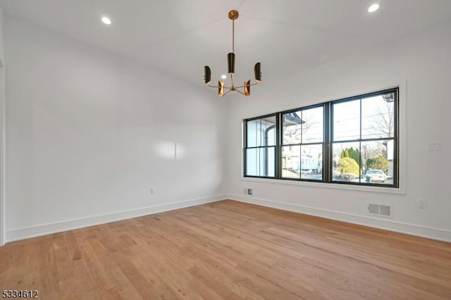 empty room with a notable chandelier and light hardwood / wood-style floors