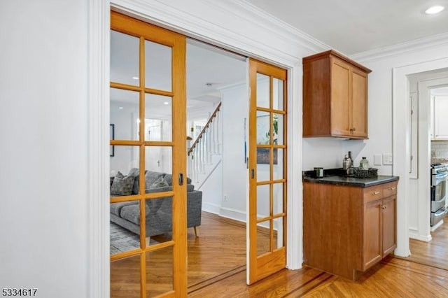 bar with french doors, ornamental molding, stainless steel range oven, and light wood-type flooring