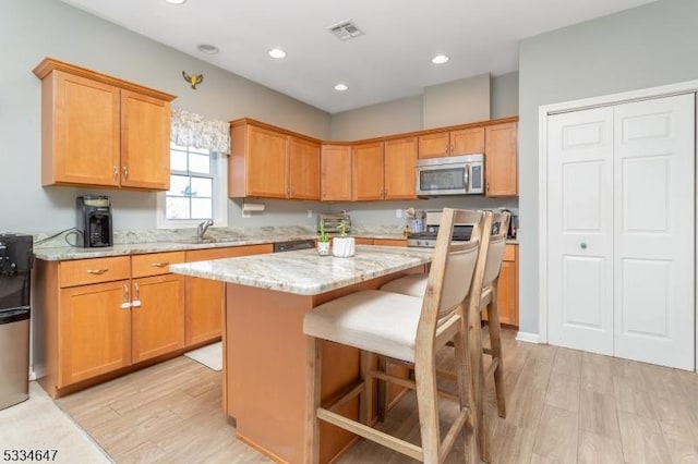 kitchen featuring sink, a breakfast bar area, light stone counters, a kitchen island, and light hardwood / wood-style floors