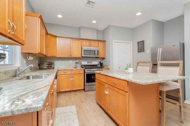 kitchen with appliances with stainless steel finishes, sink, a breakfast bar area, a center island, and light stone countertops