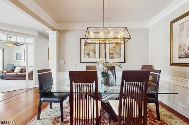 dining space featuring hardwood / wood-style flooring, ornamental molding, ceiling fan with notable chandelier, and decorative columns