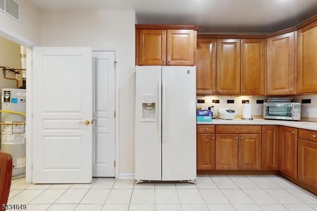 kitchen with light tile patterned floors, gas water heater, and white fridge with ice dispenser