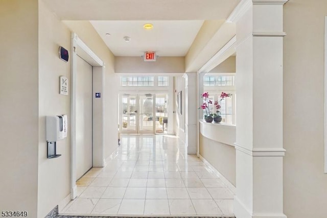 corridor featuring plenty of natural light, ornate columns, elevator, and light tile patterned flooring