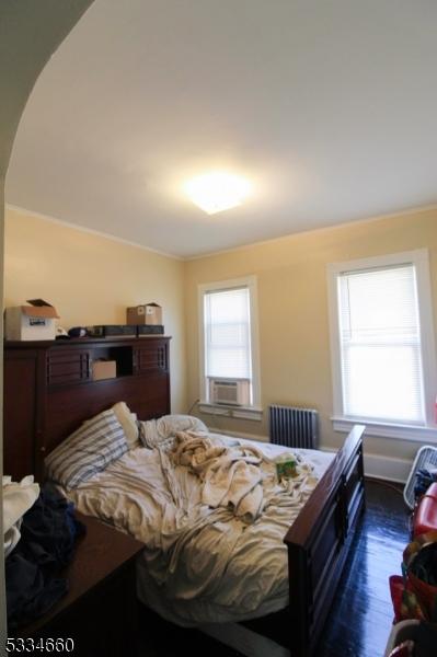 bedroom with dark wood-type flooring, radiator, multiple windows, and cooling unit