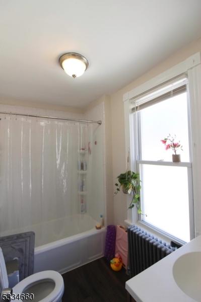 bathroom featuring radiator heating unit, toilet, shower / tub combo, and wood-type flooring