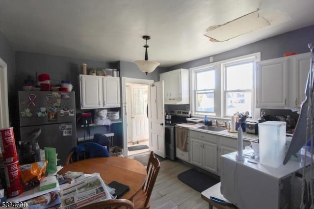 kitchen with sink, appliances with stainless steel finishes, white cabinetry, decorative light fixtures, and light wood-type flooring