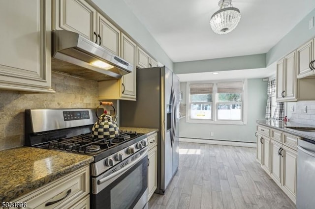 kitchen with light wood-type flooring, stainless steel appliances, cream cabinets, and dark stone countertops