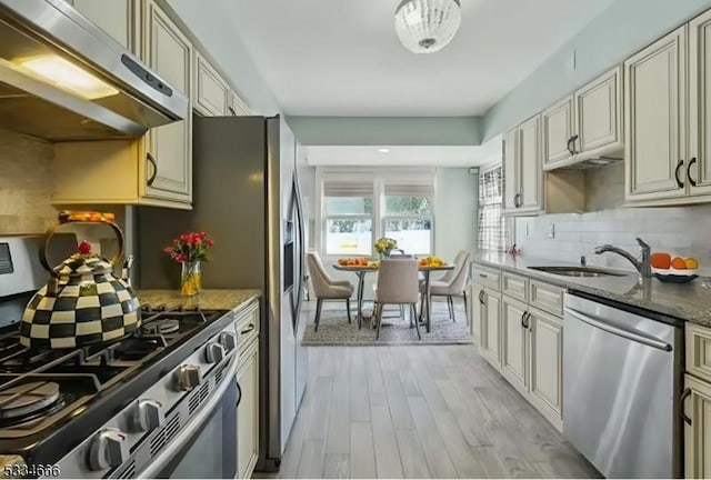 kitchen with tasteful backsplash, sink, dark stone counters, stainless steel appliances, and light wood-type flooring