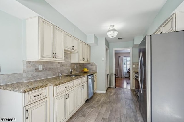 kitchen featuring sink, appliances with stainless steel finishes, tasteful backsplash, stone countertops, and light wood-type flooring