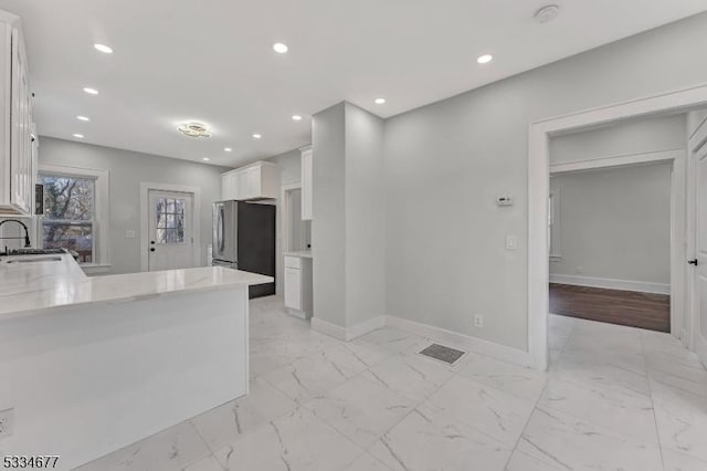 kitchen with white cabinetry, sink, stainless steel fridge, kitchen peninsula, and light stone countertops