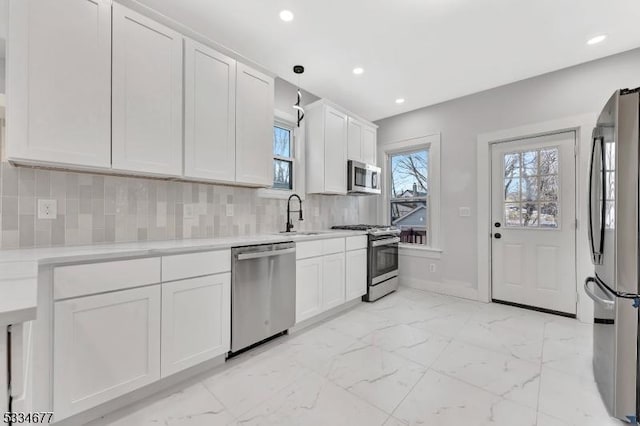 kitchen featuring sink, appliances with stainless steel finishes, backsplash, white cabinets, and decorative light fixtures