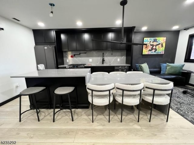 kitchen featuring sink, light hardwood / wood-style flooring, stainless steel fridge, a kitchen island, and a kitchen bar