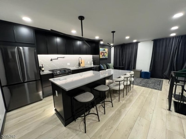 kitchen featuring sink, stainless steel fridge, hanging light fixtures, a center island, and light hardwood / wood-style flooring