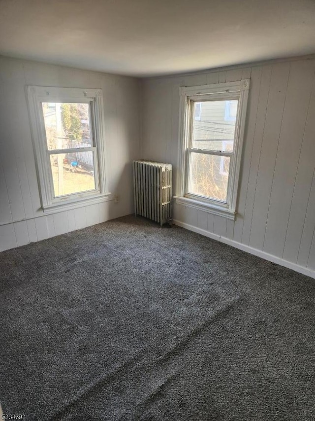 empty room featuring radiator heating unit and dark colored carpet