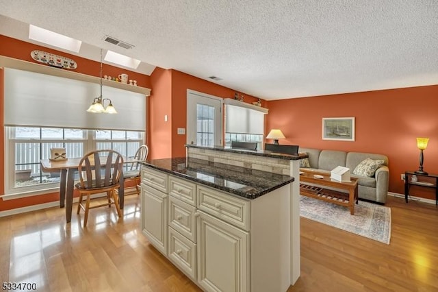 kitchen with pendant lighting, a notable chandelier, light hardwood / wood-style floors, and dark stone countertops