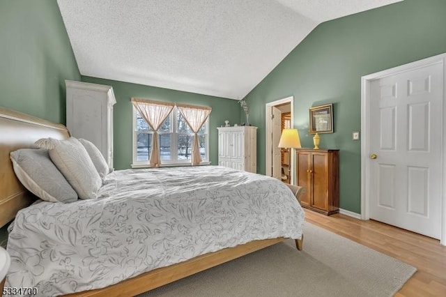 bedroom with light hardwood / wood-style flooring, vaulted ceiling, and a textured ceiling