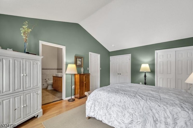 bedroom featuring lofted ceiling, ensuite bathroom, light hardwood / wood-style flooring, and two closets