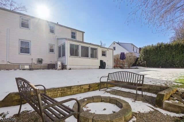 snow covered house with a sunroom, cooling unit, and a fire pit