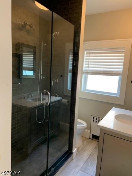 bathroom with a shower with door, vanity, radiator heating unit, and toilet