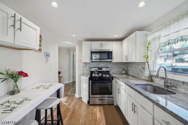 kitchen featuring sink, appliances with stainless steel finishes, white cabinetry, backsplash, and light stone counters