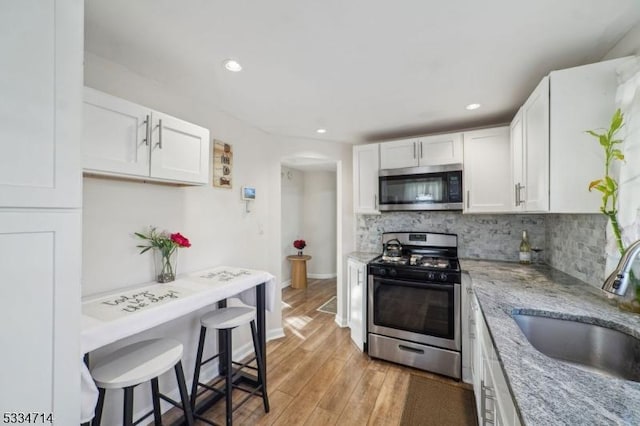 kitchen with sink, appliances with stainless steel finishes, white cabinetry, light stone counters, and decorative backsplash