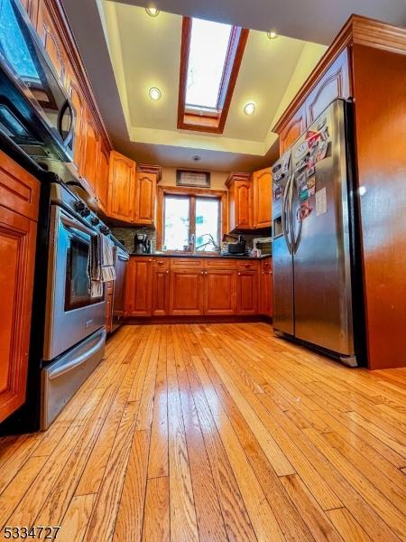 kitchen with a skylight, wall oven, a tray ceiling, light hardwood / wood-style floors, and stainless steel refrigerator with ice dispenser