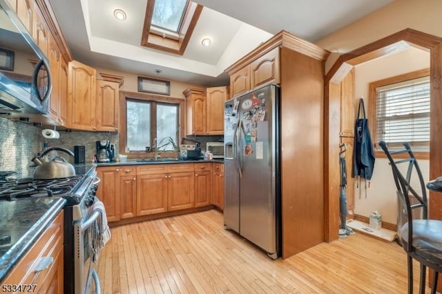 kitchen with sink, light wood-type flooring, stainless steel appliances, vaulted ceiling with skylight, and decorative backsplash