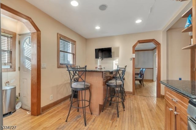 kitchen featuring a kitchen bar, light hardwood / wood-style floors, and dark stone countertops