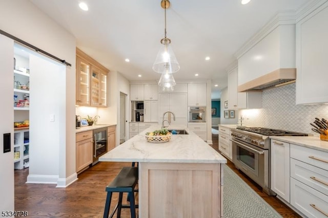 kitchen with appliances with stainless steel finishes, an island with sink, custom exhaust hood, and white cabinets