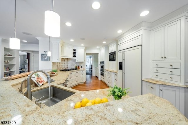 kitchen with pendant lighting, white cabinetry, sink, built in appliances, and light stone countertops