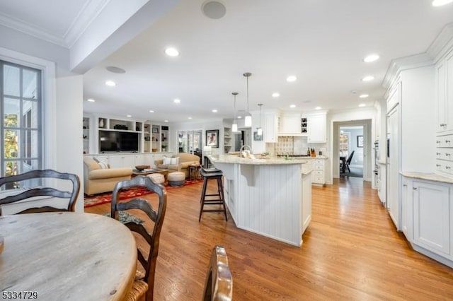 kitchen featuring white cabinetry, crown molding, hanging light fixtures, and a center island with sink