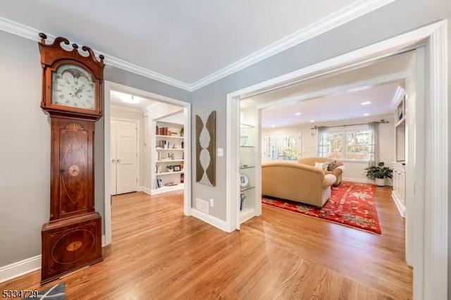 living room featuring built in shelves, ornamental molding, and light hardwood / wood-style floors