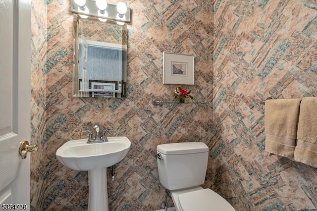 half bathroom with toilet and wallpapered walls