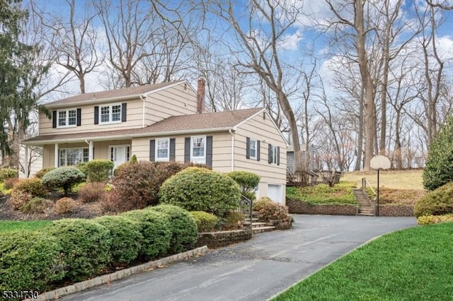 view of front of home featuring stairway, driveway, an attached garage, and a chimney