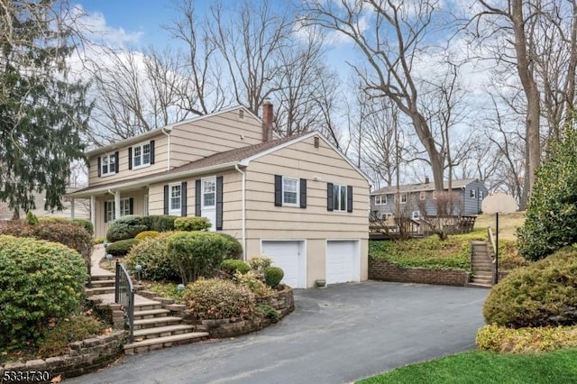 view of front of house featuring stairs, an attached garage, driveway, and a chimney