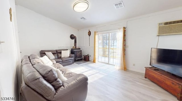 living room with a wall mounted AC, light hardwood / wood-style floors, and a wood stove