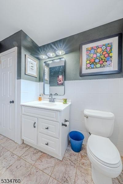 bathroom featuring vanity, toilet, and tile walls