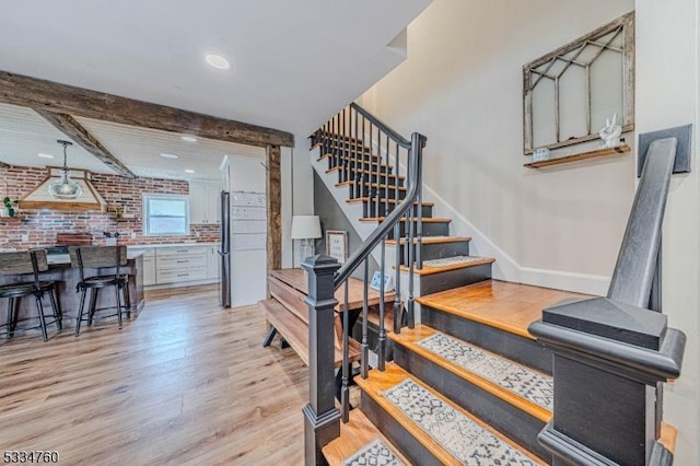 stairway with brick wall, beam ceiling, and hardwood / wood-style floors