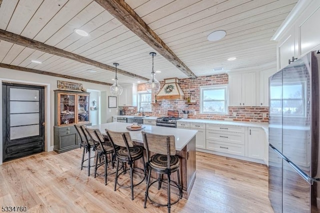 kitchen with stainless steel refrigerator, white cabinets, a kitchen island, wooden ceiling, and beamed ceiling