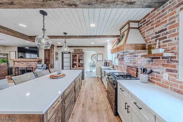 kitchen featuring range with gas cooktop, white cabinetry, a brick fireplace, hanging light fixtures, and light hardwood / wood-style flooring