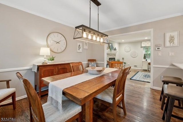 dining space featuring a fireplace, dark wood-type flooring, crown molding, and baseboards