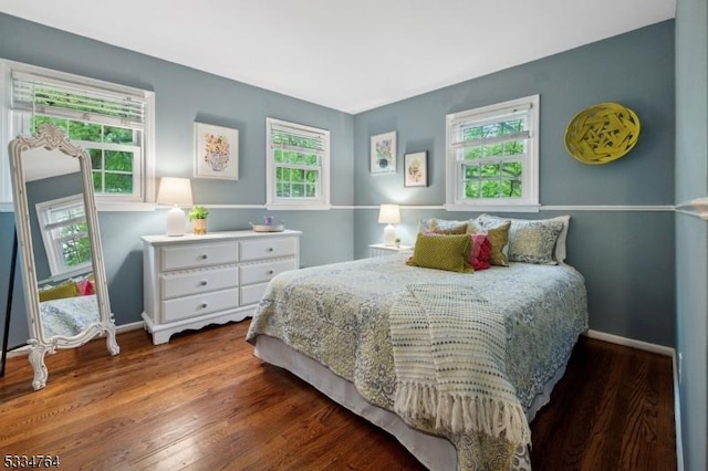 bedroom with multiple windows, wood finished floors, and baseboards