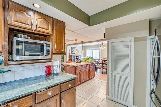 kitchen with light tile patterned floors, appliances with stainless steel finishes, tasteful backsplash, a notable chandelier, and decorative light fixtures