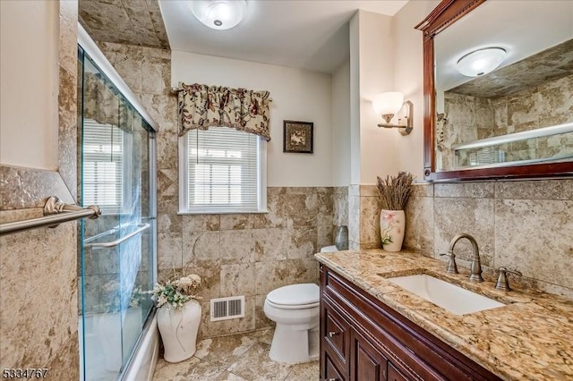 full bathroom featuring shower / bath combination with glass door, vanity, toilet, and tile walls