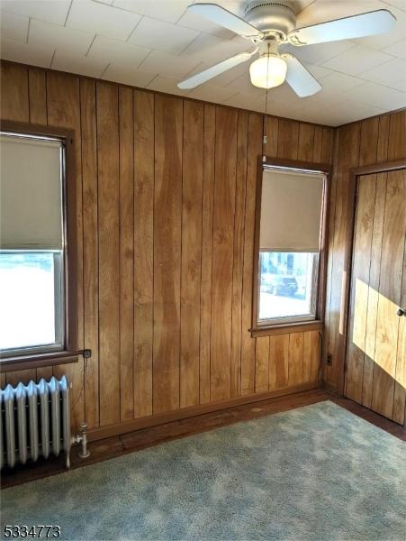 unfurnished room with ceiling fan, carpet, radiator, and wooden walls