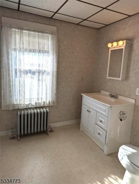 bathroom with a paneled ceiling, radiator heating unit, toilet, and vanity