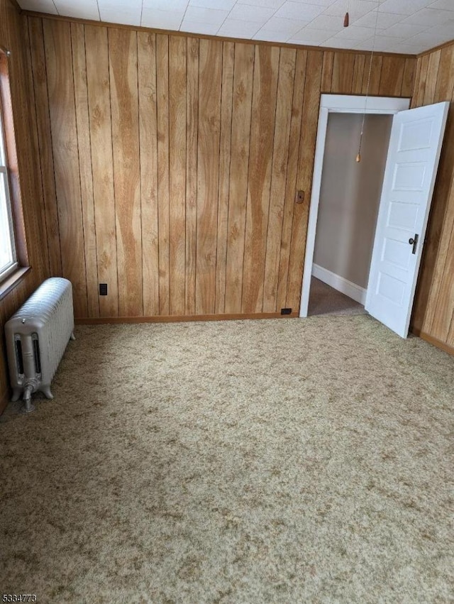 spare room featuring carpet, radiator heating unit, and wooden walls