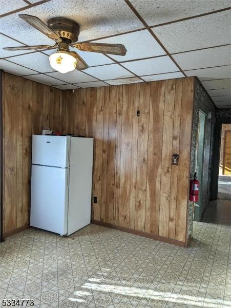 kitchen featuring white refrigerator, a paneled ceiling, ceiling fan, and wood walls