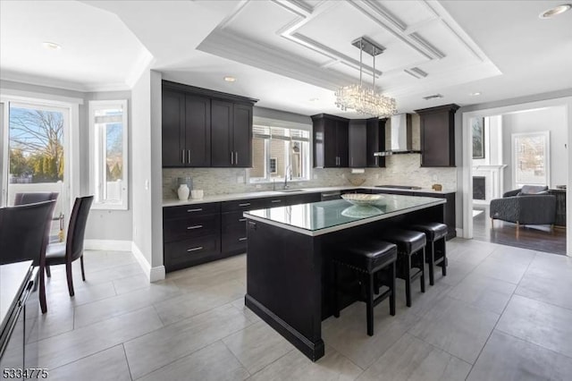 kitchen featuring a kitchen island, a kitchen bar, hanging light fixtures, black cooktop, and wall chimney exhaust hood