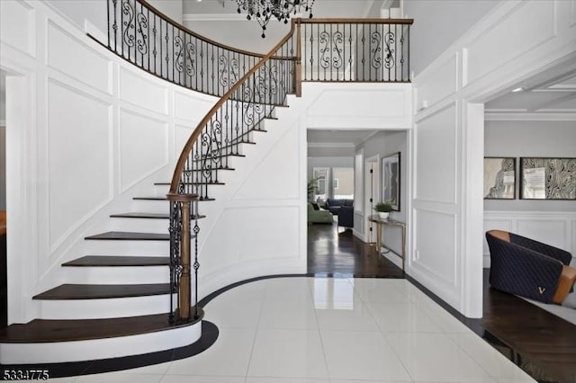 staircase featuring a high ceiling, ornamental molding, tile patterned flooring, and a chandelier